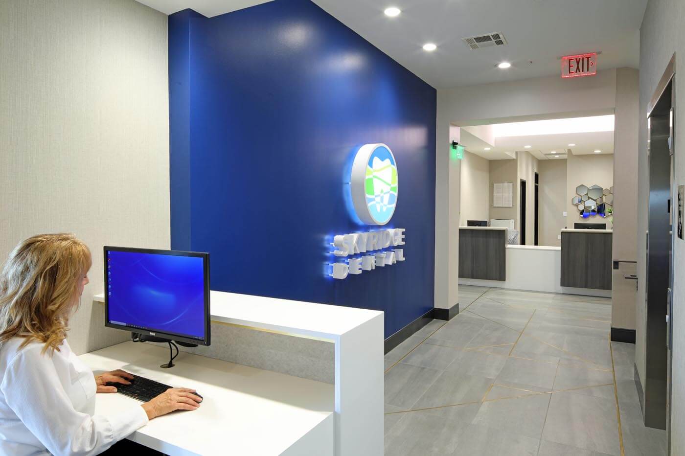 A staff member at work in the SkyRidge dental office, which is clean, modern, and sleek. At the end of the hall the reception desk can be seen.