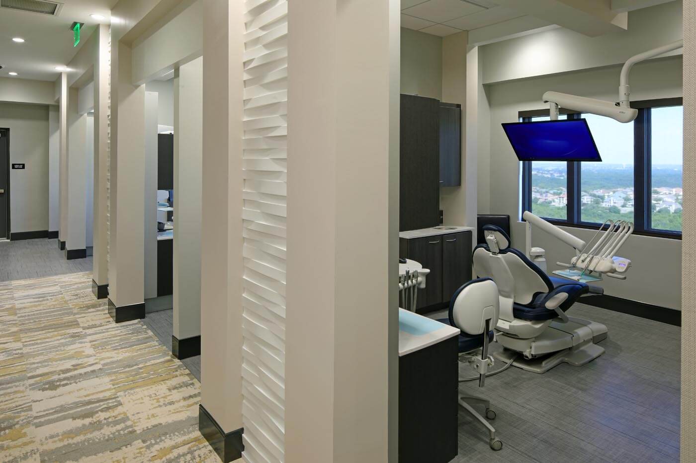A view of the office hallway, with soft but ample ambient lighting, and part of a sleek, modern exam room visible on the right.