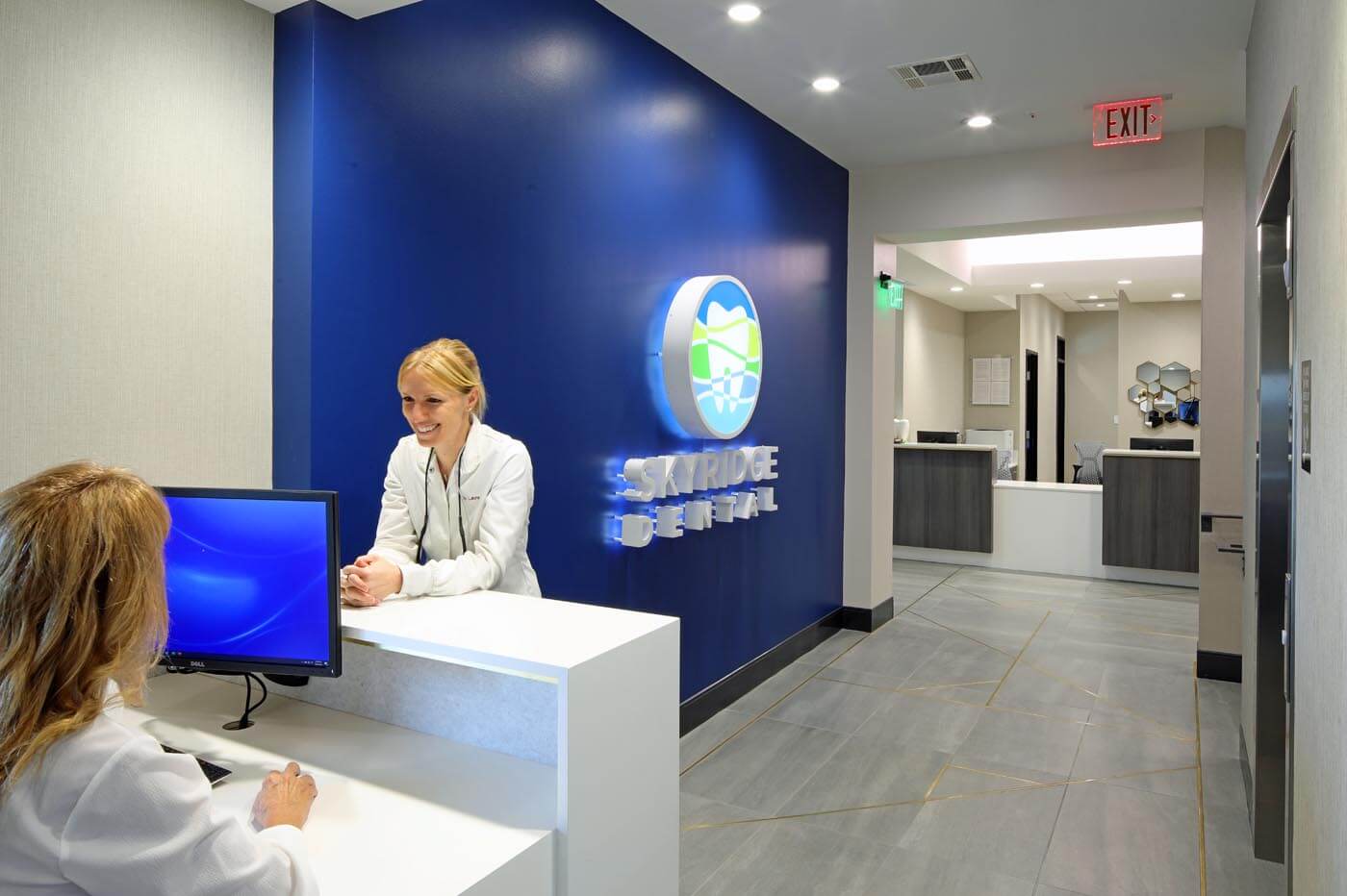 Dr. Cook talks with a staff member in a clean, modern office. An accent wall is painted blue and features a softly glowing SkyRidge Dental sign.